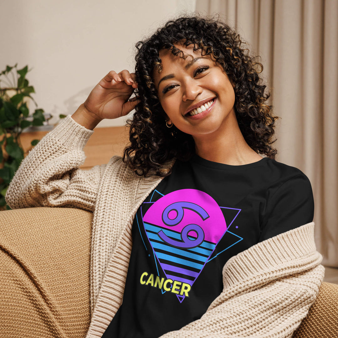 Smiling woman wearing cancer retro 80s astrology shirt with pink sun design while lounging on couch