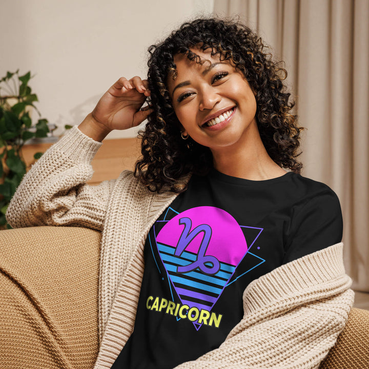Smiling woman wearing capricorn retro 80s astrology shirt with pink sun design while lounging on couch