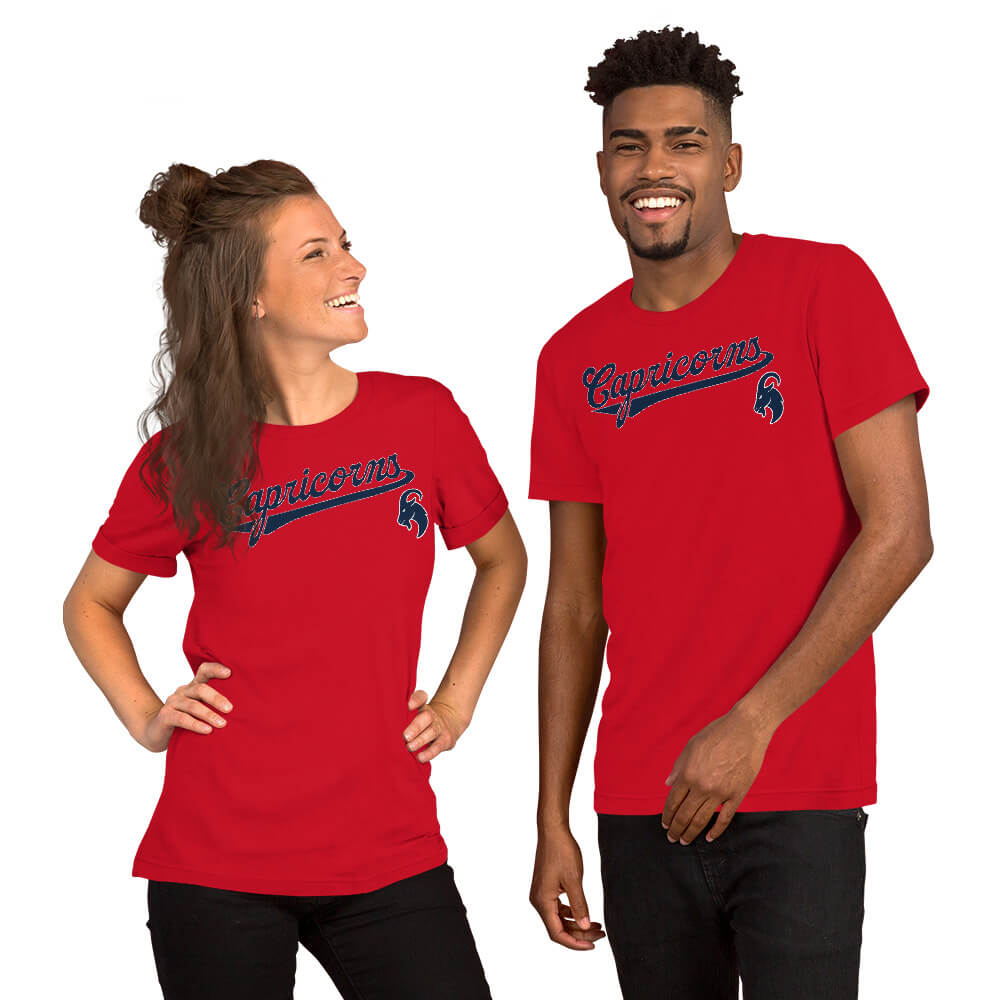 A man and a woman modeling matching red short-sleeve t-shirts with a navy and red 'Capricorns' script logo and graphic on the chest, set against a plain white background.