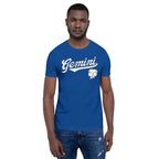 A man wearing a royal blue crewneck t-shirt with a white 'Gemini' script and graphic on the chest, paired with blue jeans, set against a plain white background.