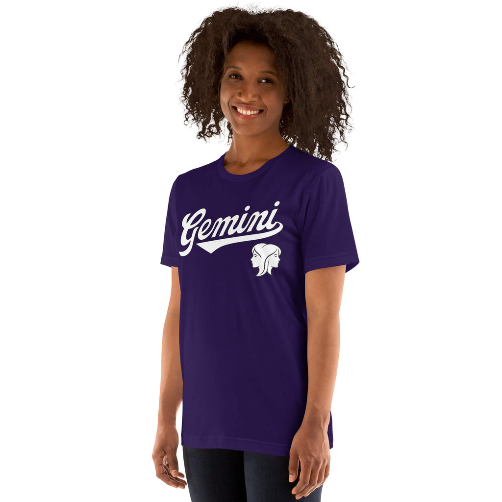 A woman with curly dark hair wearing a purple short-sleeve t-shirt with 'Gemini' in white script and a white Gemini zodiac symbol on the chest, set against a plain white background.