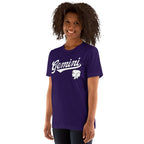 A woman with curly dark hair wearing a purple short-sleeve t-shirt with 'Gemini' in white script and a white Gemini zodiac symbol on the chest, set against a plain white background.