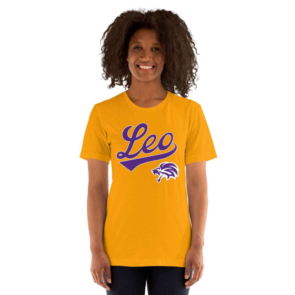 A smiling woman with curly dark hair wearing a gold short-sleeve t-shirt with a purple 'Leo' script and lion graphic on the front, set against a plain white background.