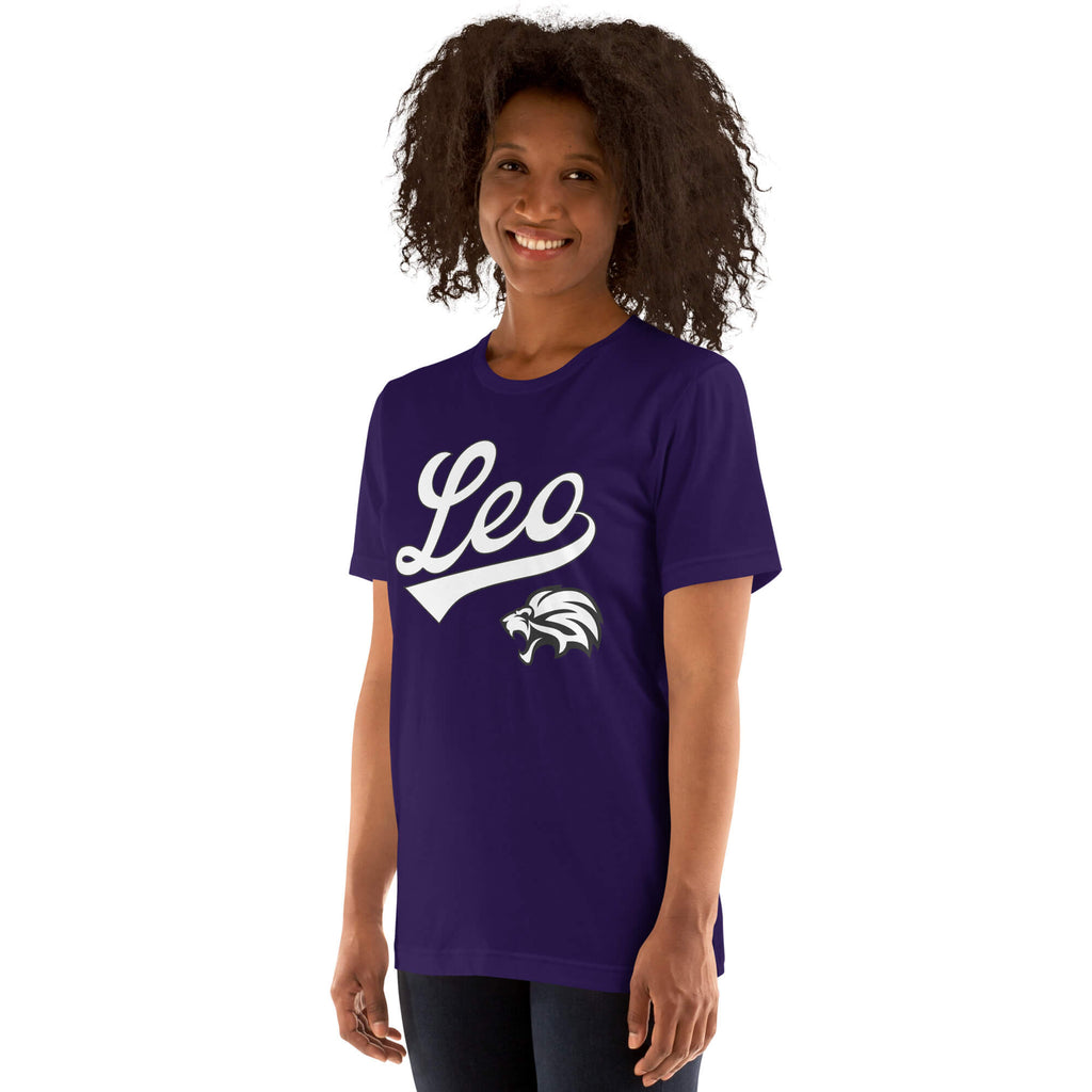 A woman with curly dark hair wearing a purple short-sleeve t-shirt with a white 'Leo' script and wildcat graphic on the front, photographed against a plain white background.