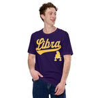 A man wearing a dark purple t-shirt with a gold 'Libra' graphic and a small Libra zodiac symbol on the front, paired with blue jeans, against a plain white background.