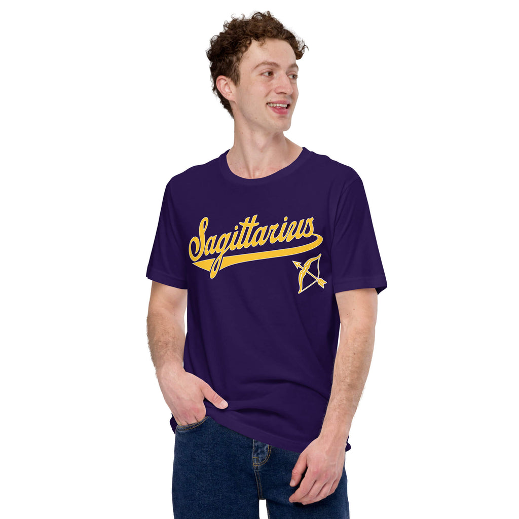 A man wearing a dark purple t-shirt with a gold 'Sagittarius' graphic and an arrow design on the chest, paired with blue jeans, set against a plain white background.