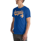 A man wearing a royal blue crewneck t-shirt with a orange 'Scorpio' graphic and zodiac symbol on the chest, shown from the waist up against a plain white background.