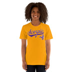 A smiling woman with curly dark hair wearing a bright gold t-shirt with a purple 'Scorpio' and scorpion graphic on the chest, set against a plain white background.
