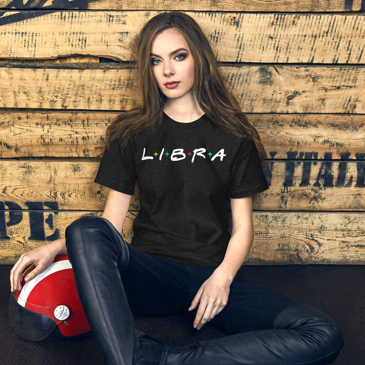 Woman wearing a black 'LIBRA' t-shirt sitting against a wooden wall with a helmet on the ground.