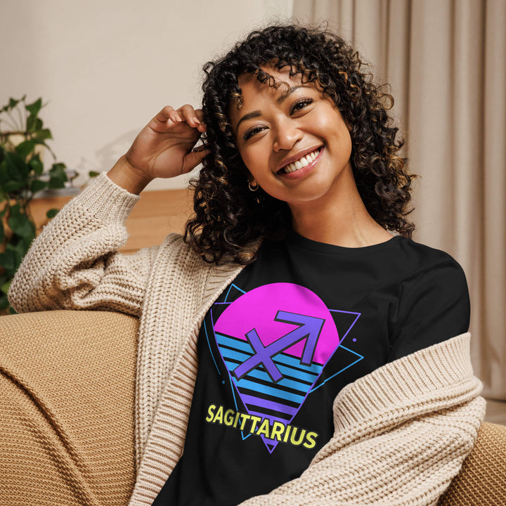 Smiling woman wearing sagittarius retro 80s astrology shirt with pink sun design while lounging on couch